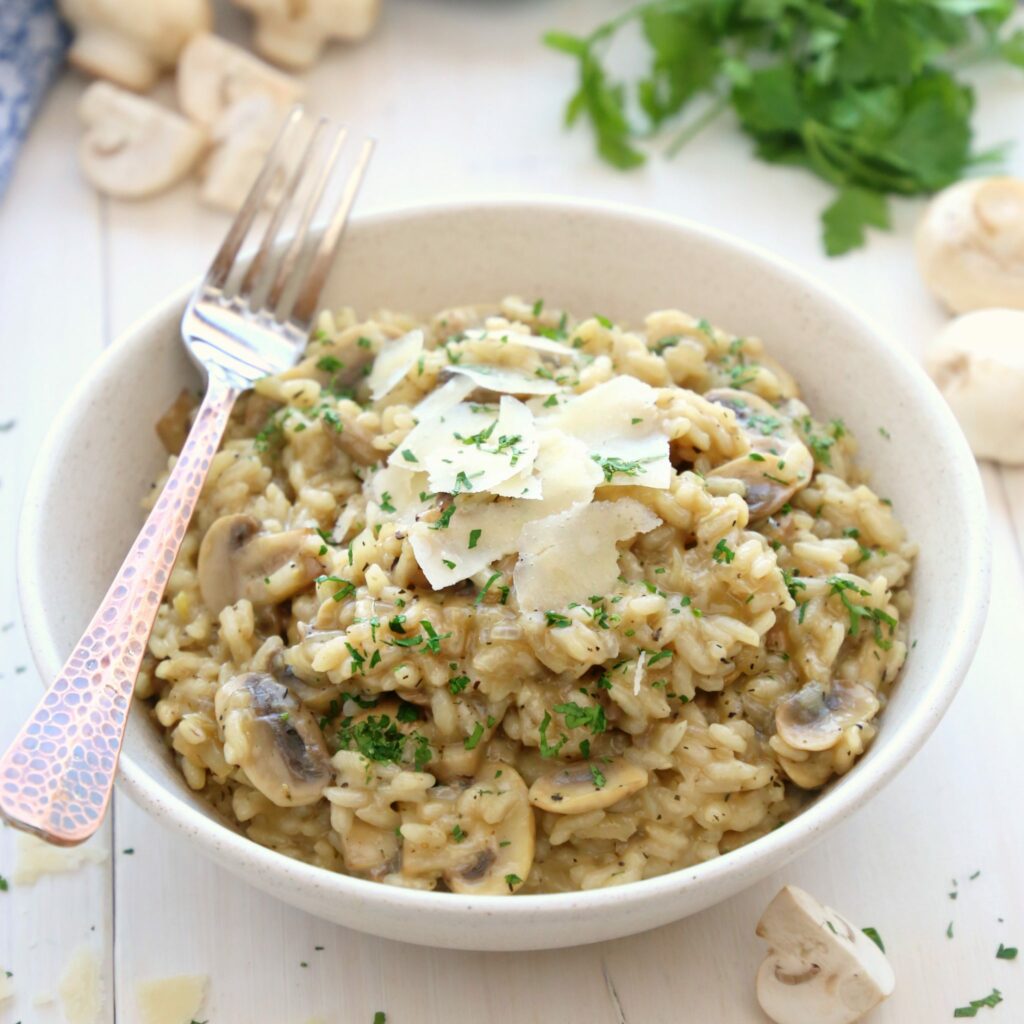 Psychedelic mushrooms risotto on a white plate on a white table with mushrooms and greens