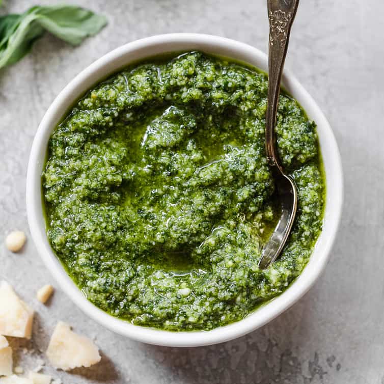 Psylocibin mushrooms pesto in a white bowl placed on a table with basil and parmesan